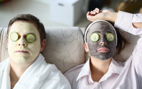Top view of wife and husband wearing cleaning face masks. Relaxed woman and man laying on sofa. Couple with cucumber slices on eyes. Spare time at home and cosmetology concept